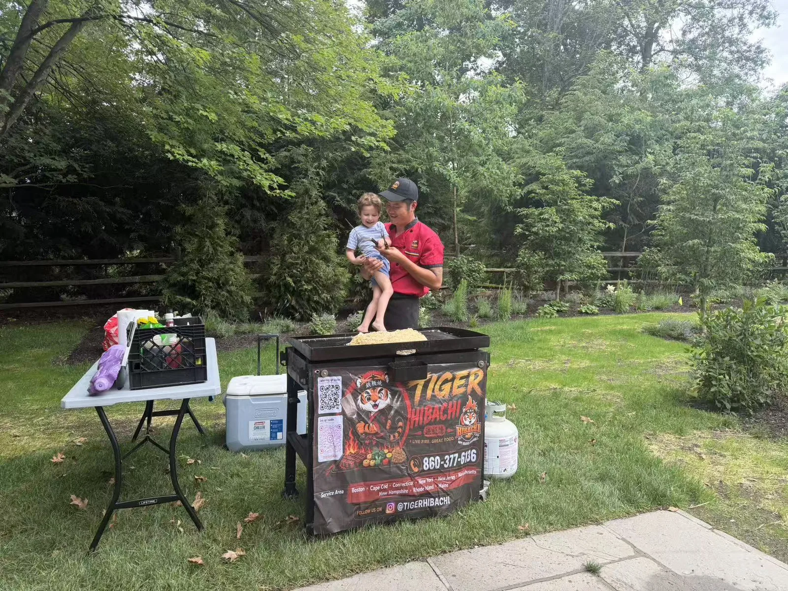 Tiger Hibachi chef cooking fried rice on a mobile teppanyaki griddle at a Glastonbury CT backyard party while holding a toddler
